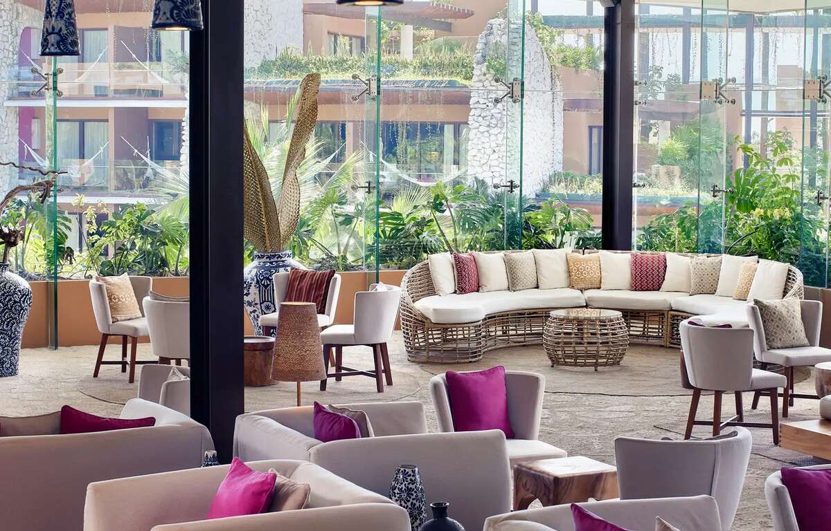 Armchairs in a lobby. A hotel building is transparent through the windows. Woven palm leaf decoration.