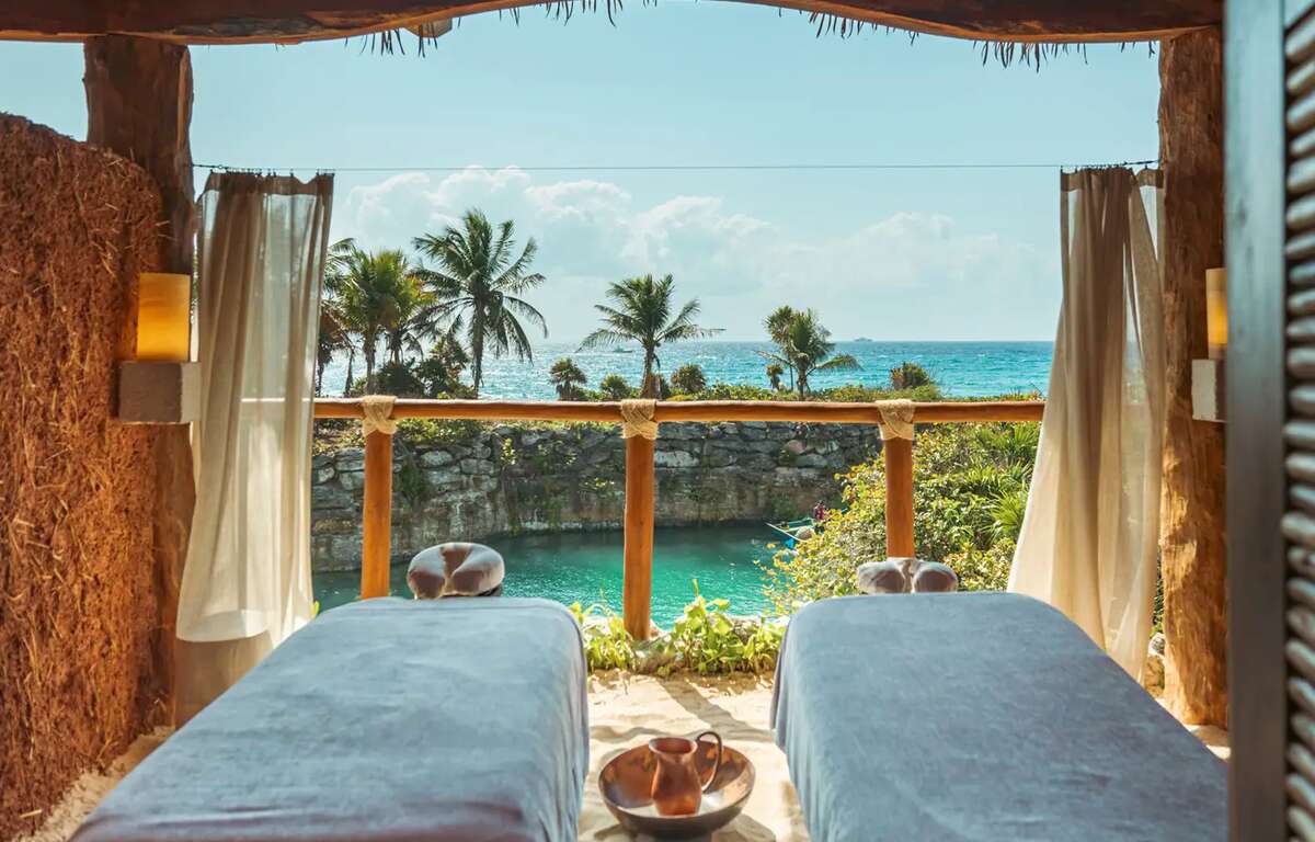 Two spa beds overlooking the Caribbean Sea. Blue sky and palm trees in the background. Soft light around the beds.