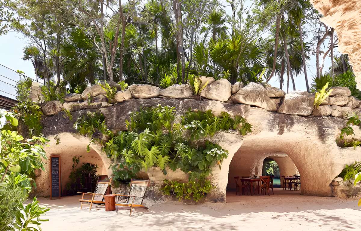 A restaurant carved into the rock with many green areas around and above it.