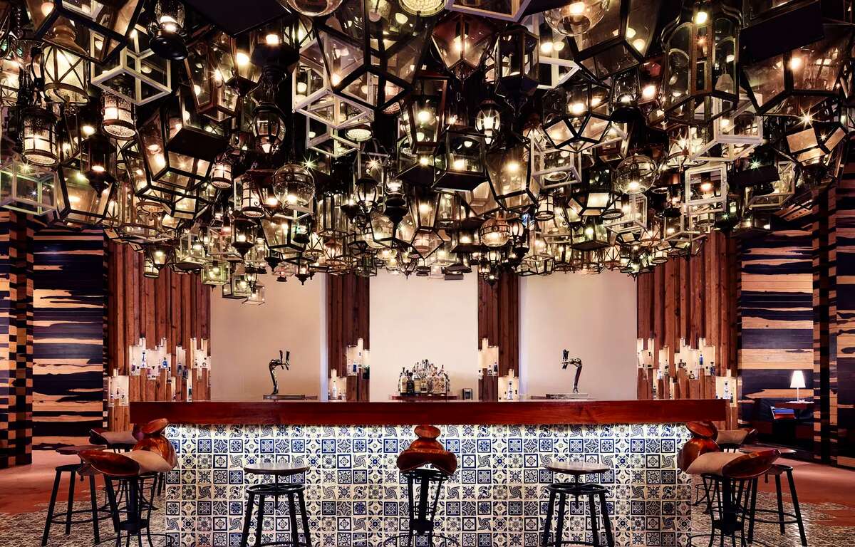 The bar of a bar covered in mosaic. A large number of lanterns hang from the ceiling. Stools in front of the bar.