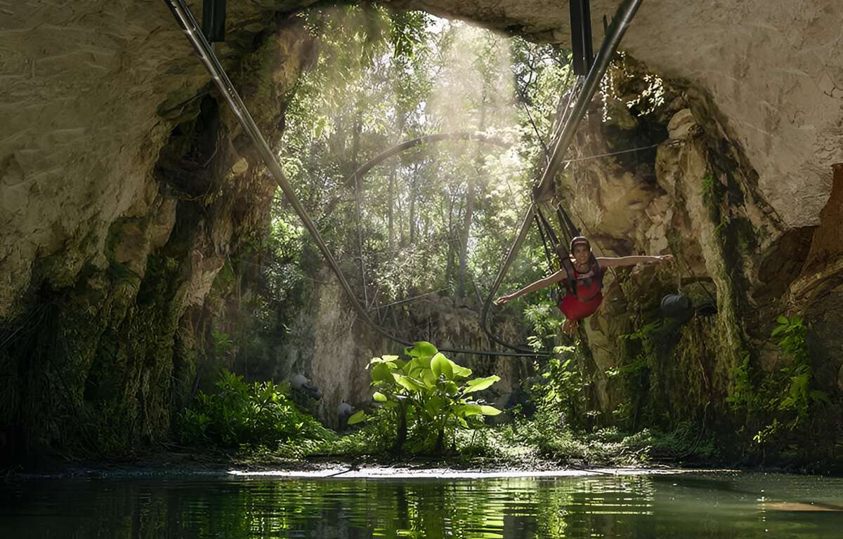 A zip line entering a cave. The person on the zip line is almost lying down with his head forward.